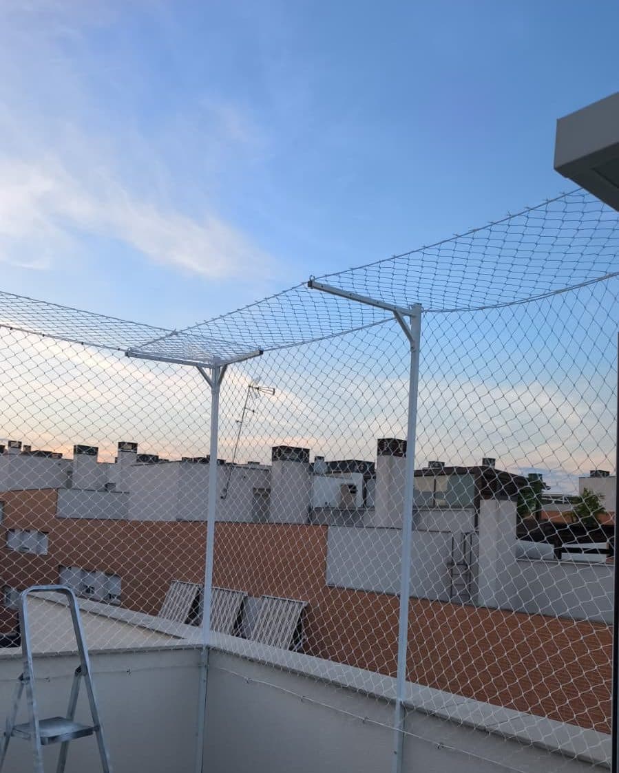 Terraza de ático con postes blancos y brazos superiores que inclinan la red hacia dentro