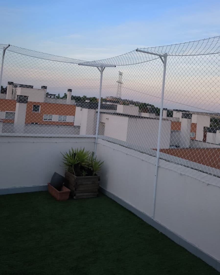Esquina de terraza con césped artificial y valla antiescape con la red inclinada hacia dentro